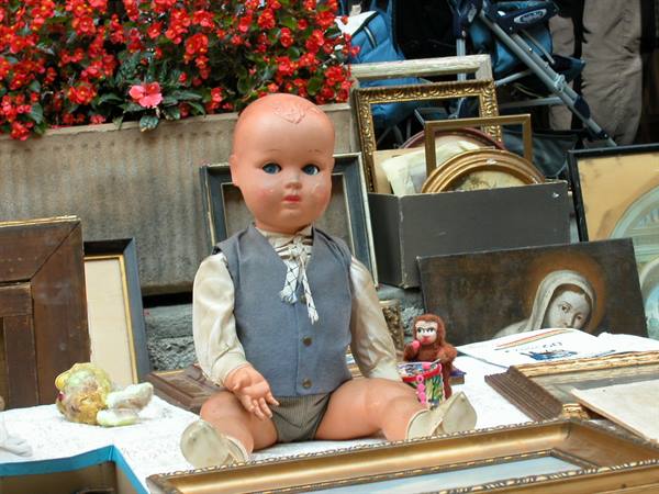 Celluloid doll sitting among gilded frames and prints at a flea market
