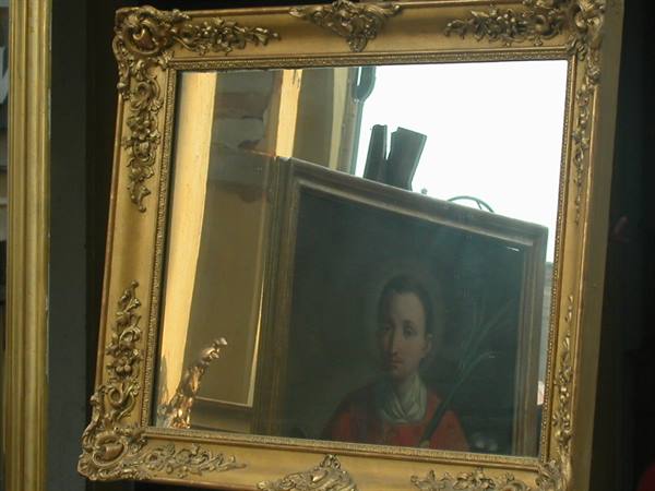 Carved gilded mirror reflecting a saint painting in a workshop