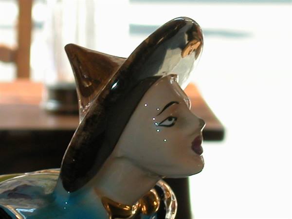 Glazed ceramic figurine of a woman wearing a wide hat, light reflecting on glossy surface