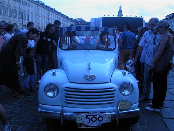 Vintage white Fiat 500 displayed in a Turin square, crowd gathered around