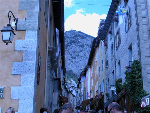 Busy street between colorful houses and rocky mountain, lantern and awnings