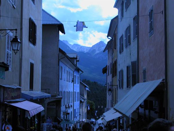 Busy street between colorful houses in Briançon, awnings and mountains behind