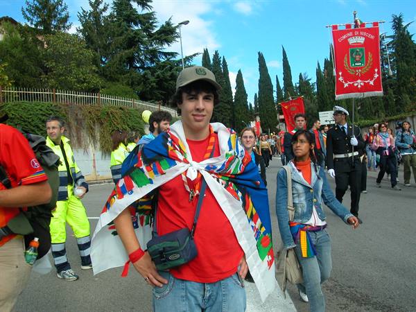 Smiling young man with a flag over his shoulder among parade crowd in Assisi