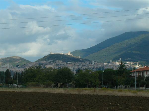 Assisi: white houses on the hillside, plowed fields and mountains under clouds