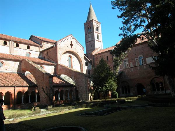 Red brick cloister with Romanesque bell tower at Staffarda Abbey, bright sunlight