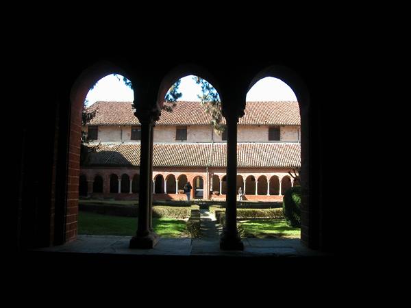 Medieval brick cloister seen through dark arches, stone columns and sunny garden