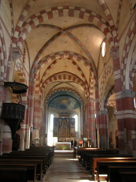 Nave with red and white brick arches, wooden pews and lit altar