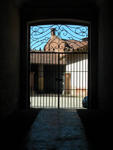 Wrought iron gate opening onto farmhouse courtyard with brick rooftops