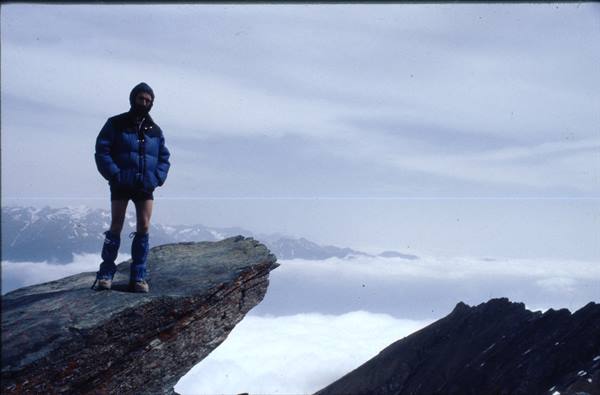 Climber in blue down jacket on snowy rock above the clouds
