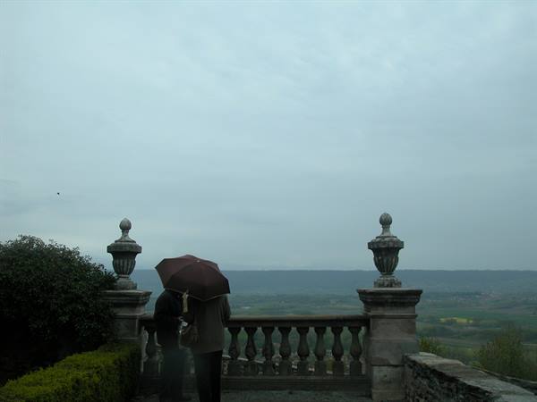 Two people under an umbrella on a stone terrace with balustrade