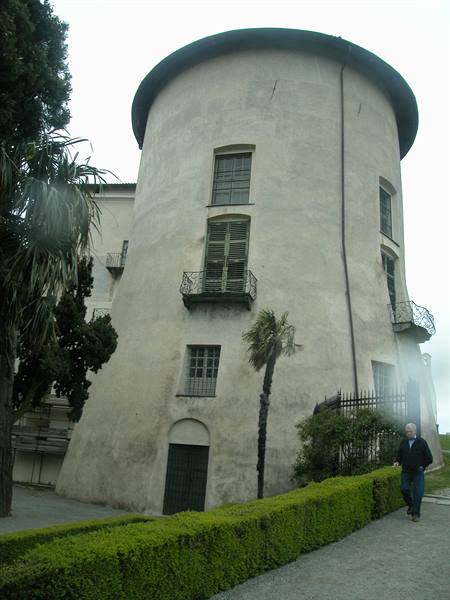 Round white-plastered tower with wrought-iron balconies, low hedge and a visitor walking