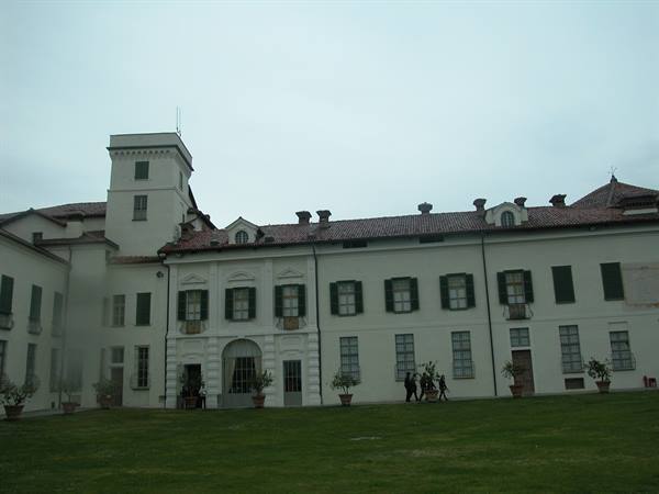 White villa with tower and green shutters, lawn in front, grey sky