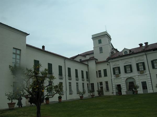 Courtyard of white villa with tower, potted citrus trees and lawn under grey sky