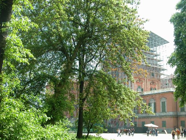 Historic brick building under scaffolding among green trees and passersby