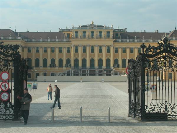 Wrought iron gate of Schönbrunn palace, pedestrians walk toward the yellow facade
