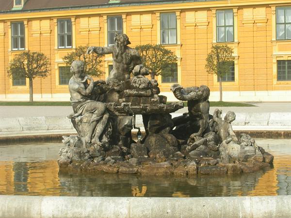 Baroque stone fountain with statues before Schönbrunn's yellow facade