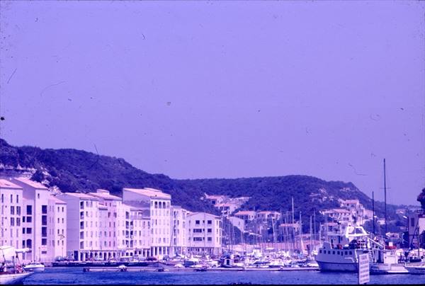 Sailboats moored in Bonifacio harbor, white buildings and cliffs under blue sky