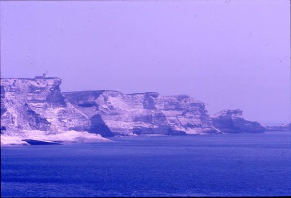 White layered cliffs above blue sea, soft light, small building on clifftop