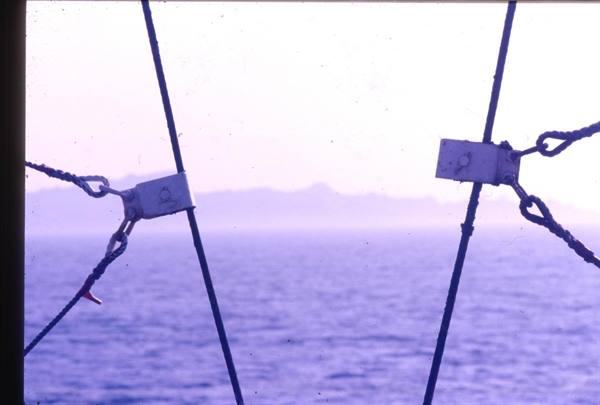 Steel cables with clamps in the foreground, sea and hazy mountains behind