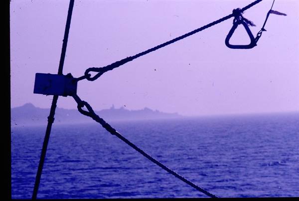 Steel ship cables and shackle against a hazy coastline at sea
