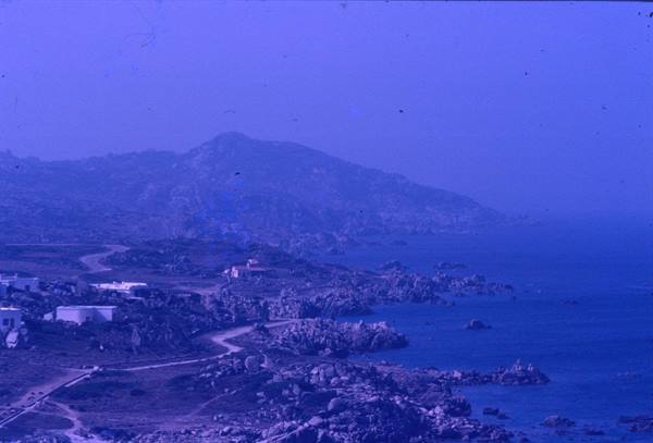 Granite coastline with rocks and white houses, road winding toward the sea