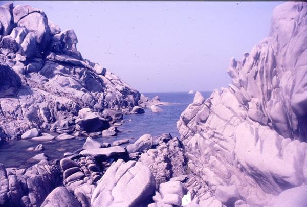 Wind-carved granite boulders plunge into a blue sea, Capo Testa