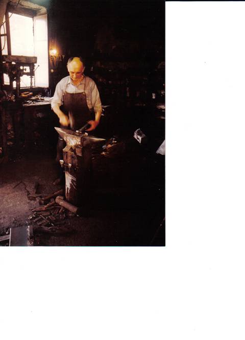 Blacksmith in leather apron hammering iron on anvil in dim workshop