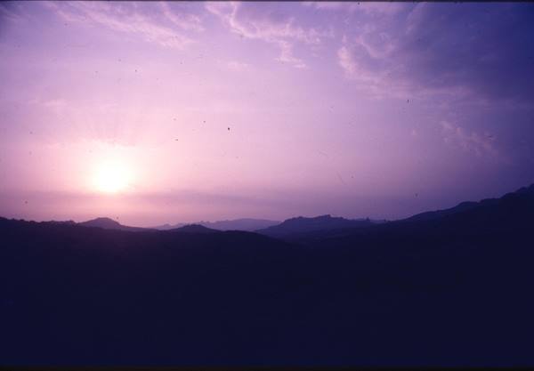 Low sun behind dark silhouette hills, purple and pink sky, grainy film