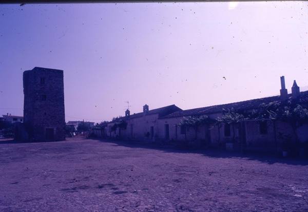 Medieval stone tower beside whitewashed houses on a dusty square
