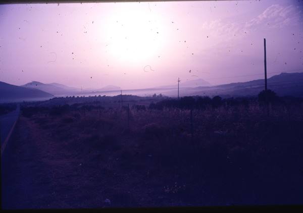 Low sun over dark hills and fields, road and poles