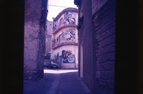 Alley between stone walls, building with painted murals and balconies