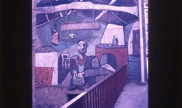 Mural of a seated man painted on a wall, beside a red railing