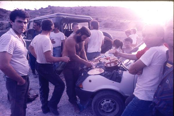 Men eating on the hood of a grey car in dry hills, low sunlight