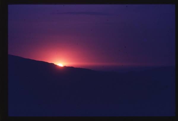 Red sun sinking behind a dark hill, purple glowing sky