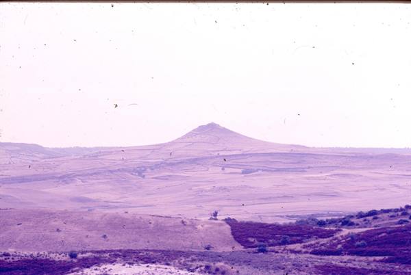 Solitary conical hill over arid plateau, faded old photograph