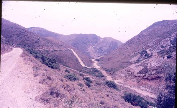 Dirt road winding down dry hills with shrubs in an old slide