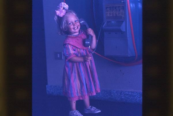 Smiling little girl with flower in hair holding phone beside a vending machine