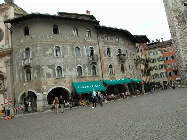 Frescoed buildings on paved square in Trento, people strolling past Caffè Italia
