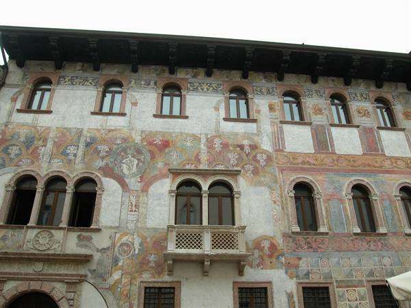 Faded frescoed facade with stone balcony and arched windows, Trento