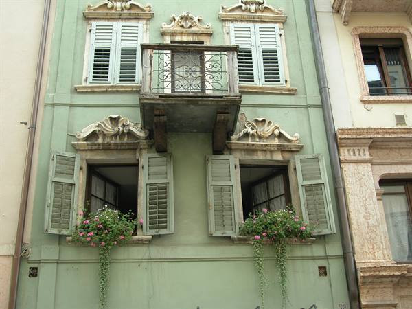Green facade with wrought iron balcony, shutters and flowers on window sills