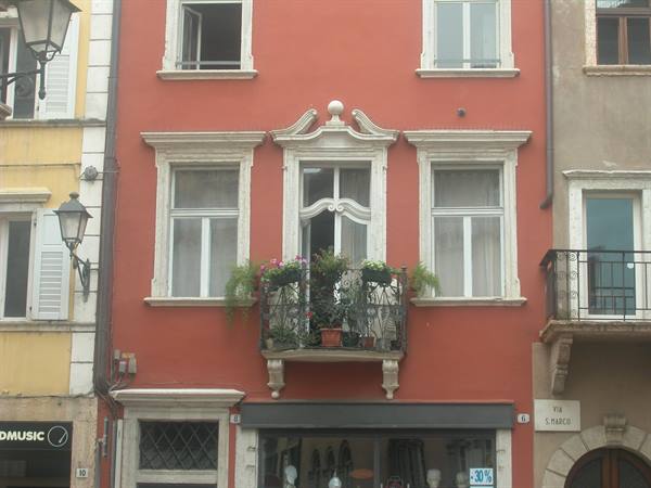 Red facade with wrought-iron balcony full of flowers, street lamp nearby