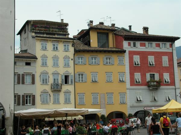 People seated at café tables under white umbrellas among old colorful buildings