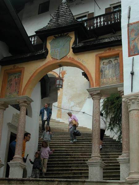 Visitors descend the frescoed staircase of Castel Tirolo, lantern hanging from the arch