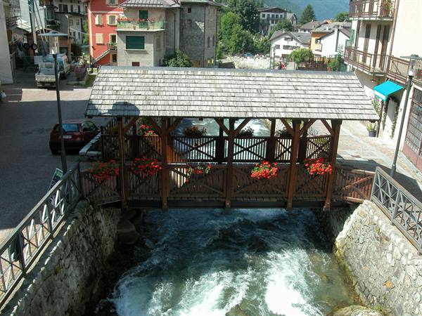 Covered wooden bridge with red flowers over rushing stream in mountain village