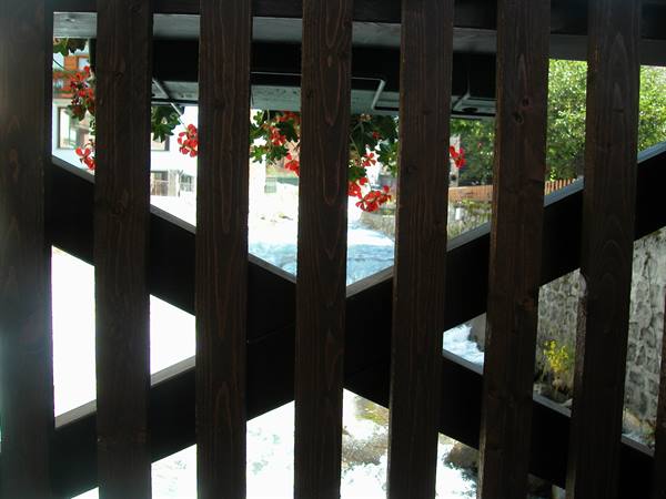 Red flowers and stream seen through the wooden railing of a covered bridge