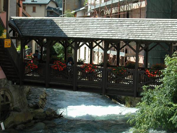 Wooden covered bridge with red geraniums over a rushing stream
