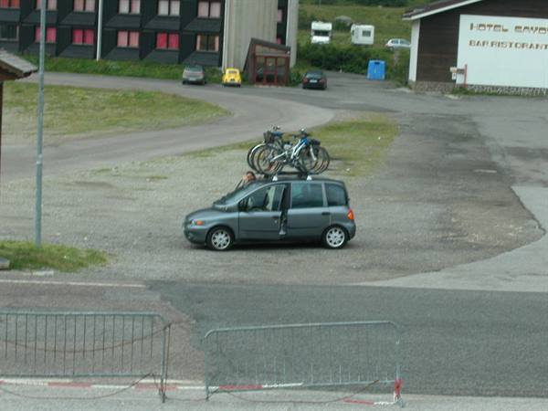 Grey car with bicycles on roof rack in front of a mountain hotel