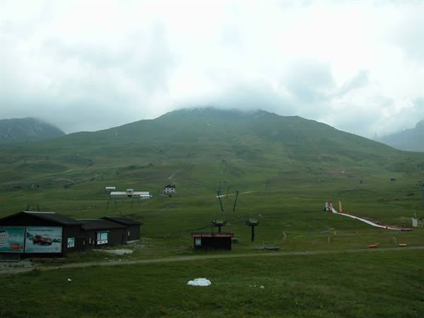 Chairlift station among green meadows, mountain shrouded in clouds and fog
