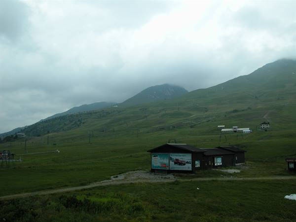 Wooden chalet with billboards on green meadow, cloud-covered mountains