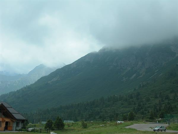 Low clouds over green mountain, wooden house and parking lot with car
